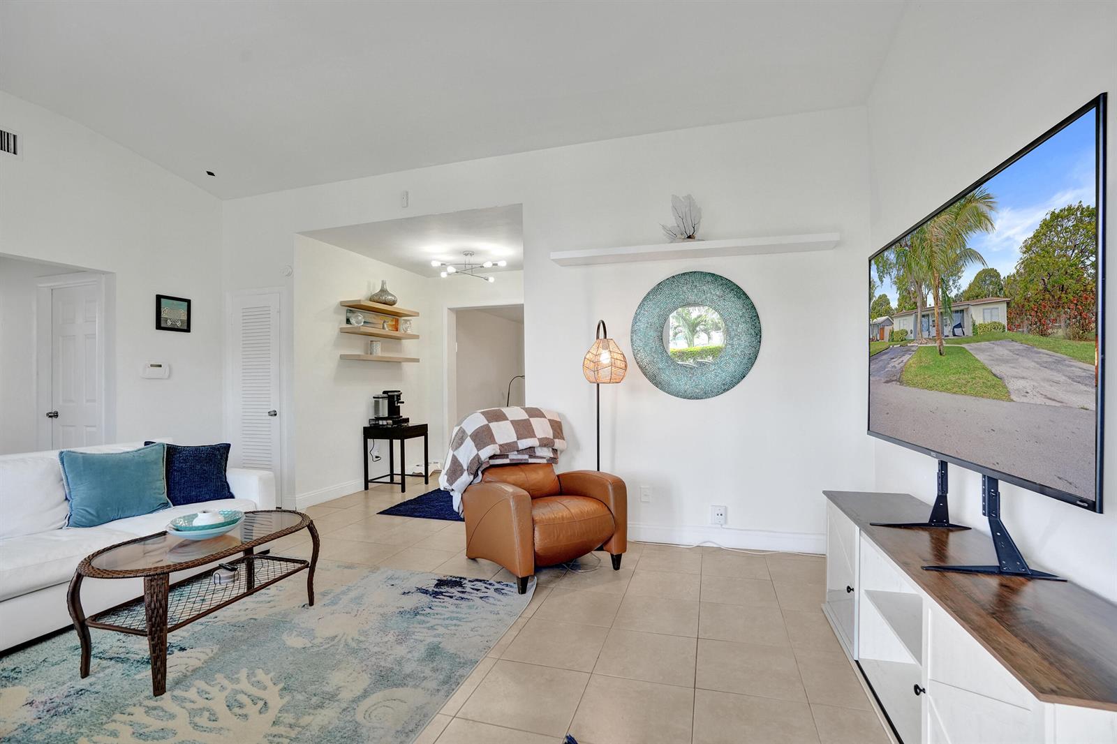 A living room features a white sofa, a leather armchair, and a large wall-mounted television — 2461 NE 20th Avenue, Lighthouse Point FL 33064, LIGHTHOUSE POINT, FL