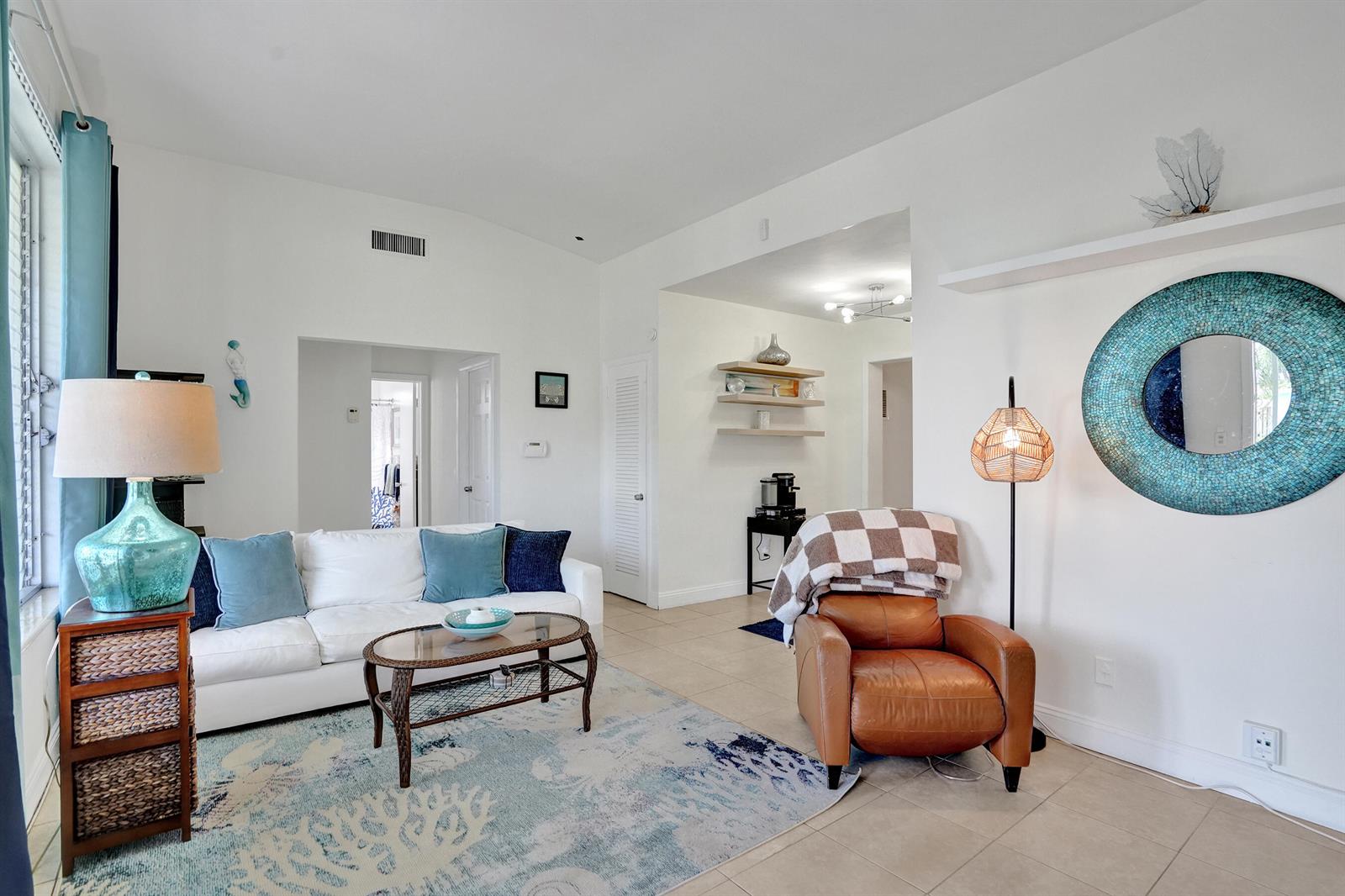 A living room features a white sofa, a leather armchair, and a blue mosaic mirror — 2461 NE 20th Avenue, Lighthouse Point FL 33064, LIGHTHOUSE POINT, FL