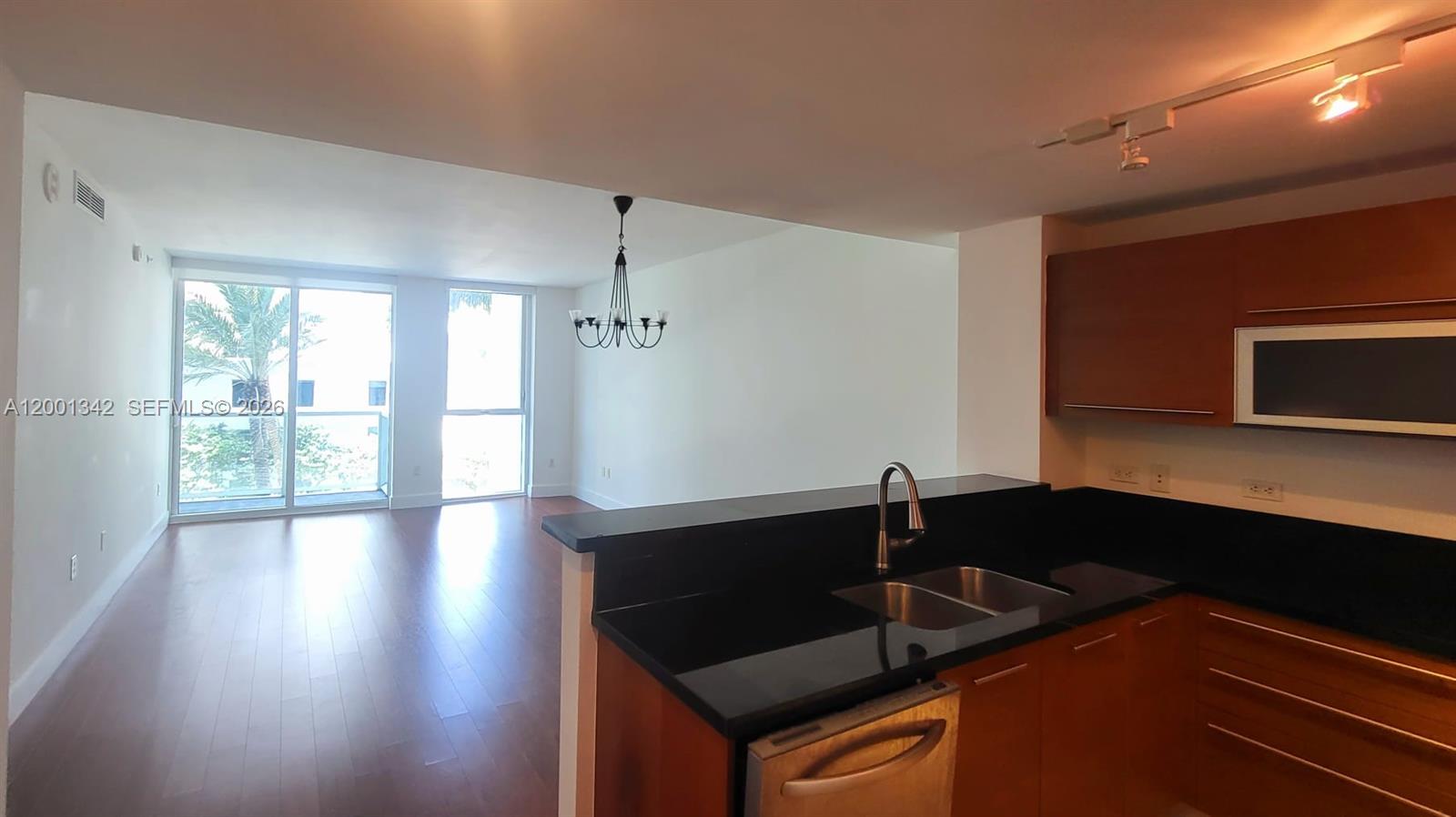 A kitchen with dark countertops and wood cabinets overlooks an open living area with hardwood floors — 253 NE 2nd St # 1004, Miami FL 33132, MIAMI, FL