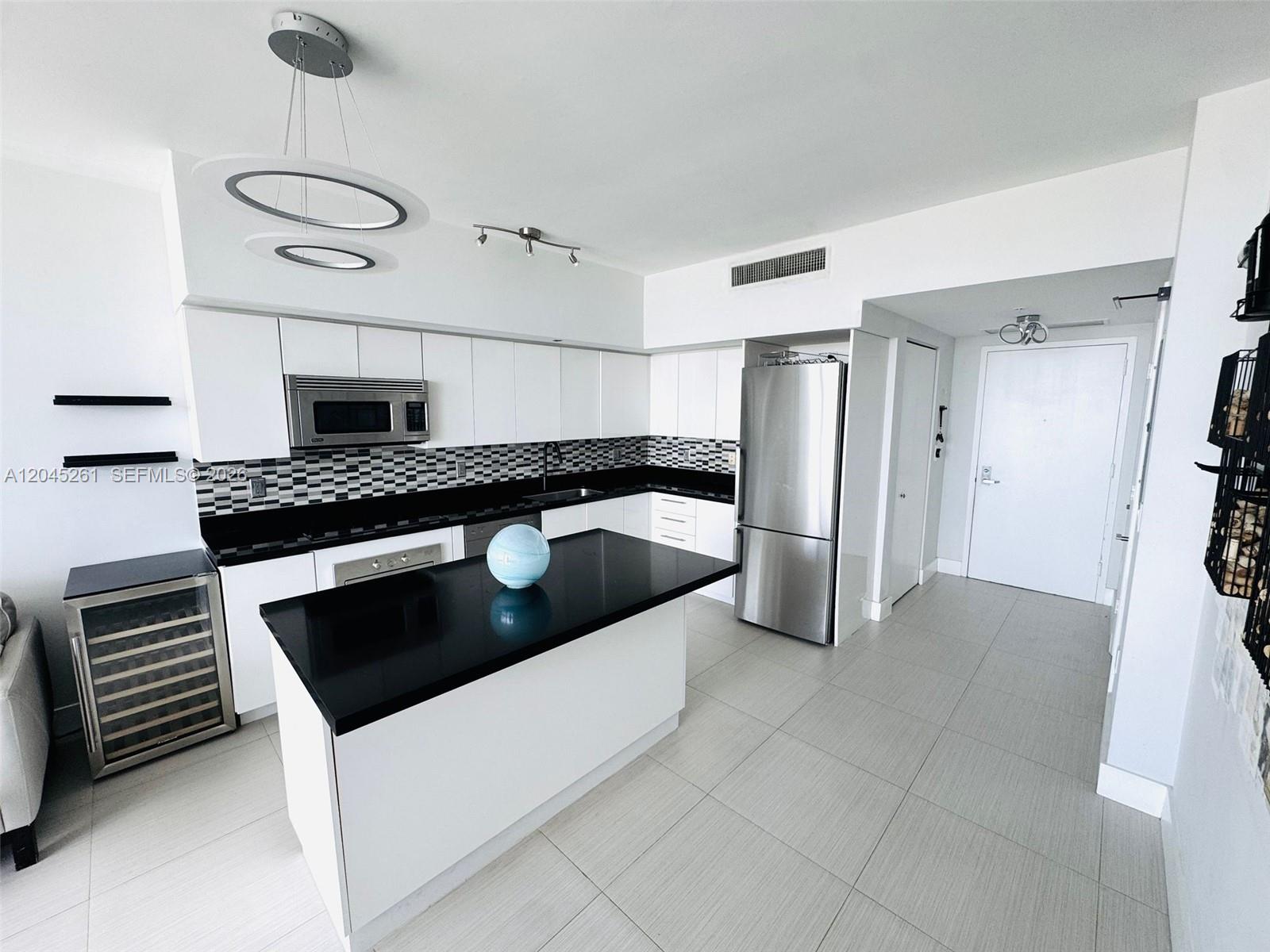 A modern kitchen features white cabinets, black countertops, a central island, and stainless steel appliances — 92 SW 3rd St # 3608, Miami FL 33130, MIAMI, FL