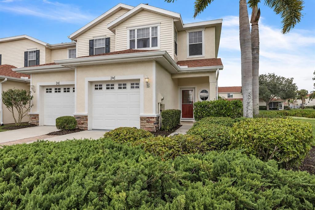 A two-story townhouse with a beige exterior, a white garage door, and a red front door — 2345 FELICITY PLACE, NORTH PORT, FL