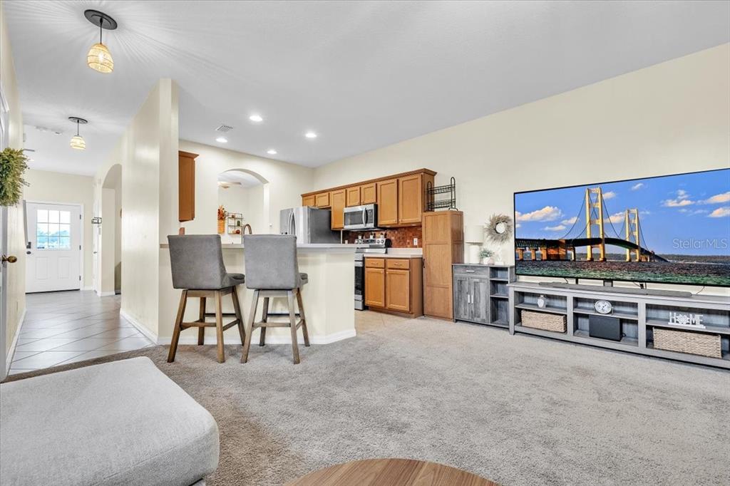 A living room with gray carpet, a large television, and an open kitchen with bar seating — 2345 FELICITY PLACE, NORTH PORT, FL