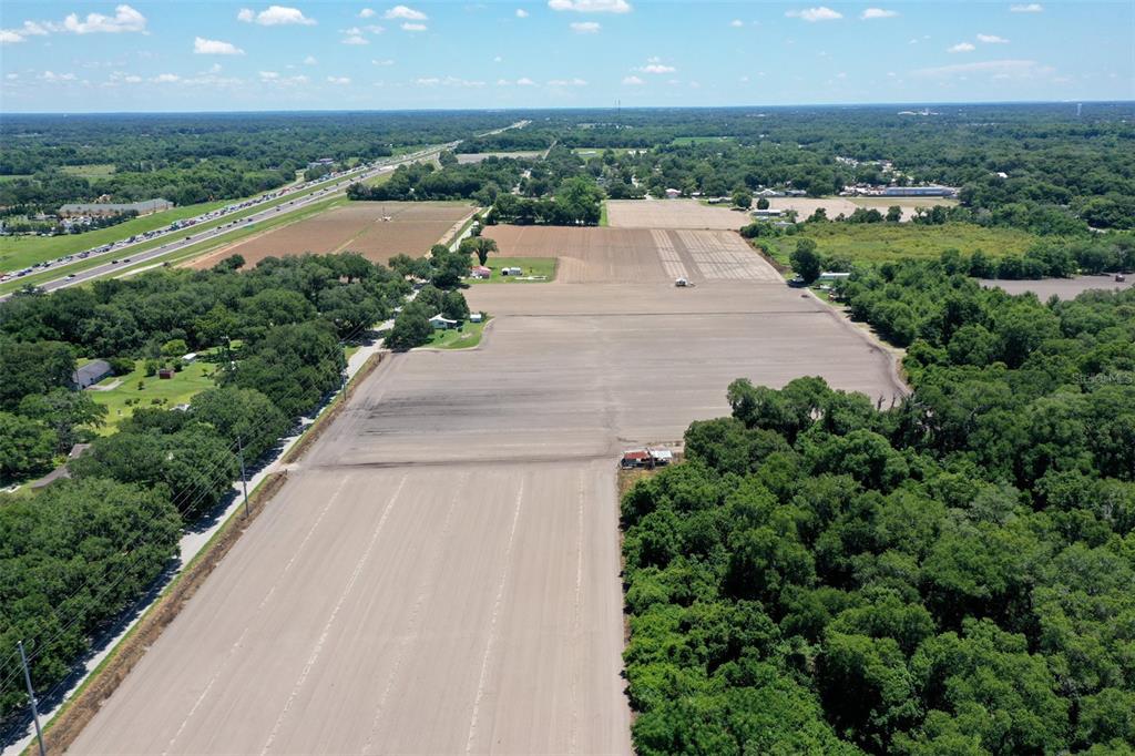 An aerial view shows a large, cleared agricultural field surrounded by dense trees and roads — 5617 GLEN HARWELL ROAD, PLANT CITY, FL