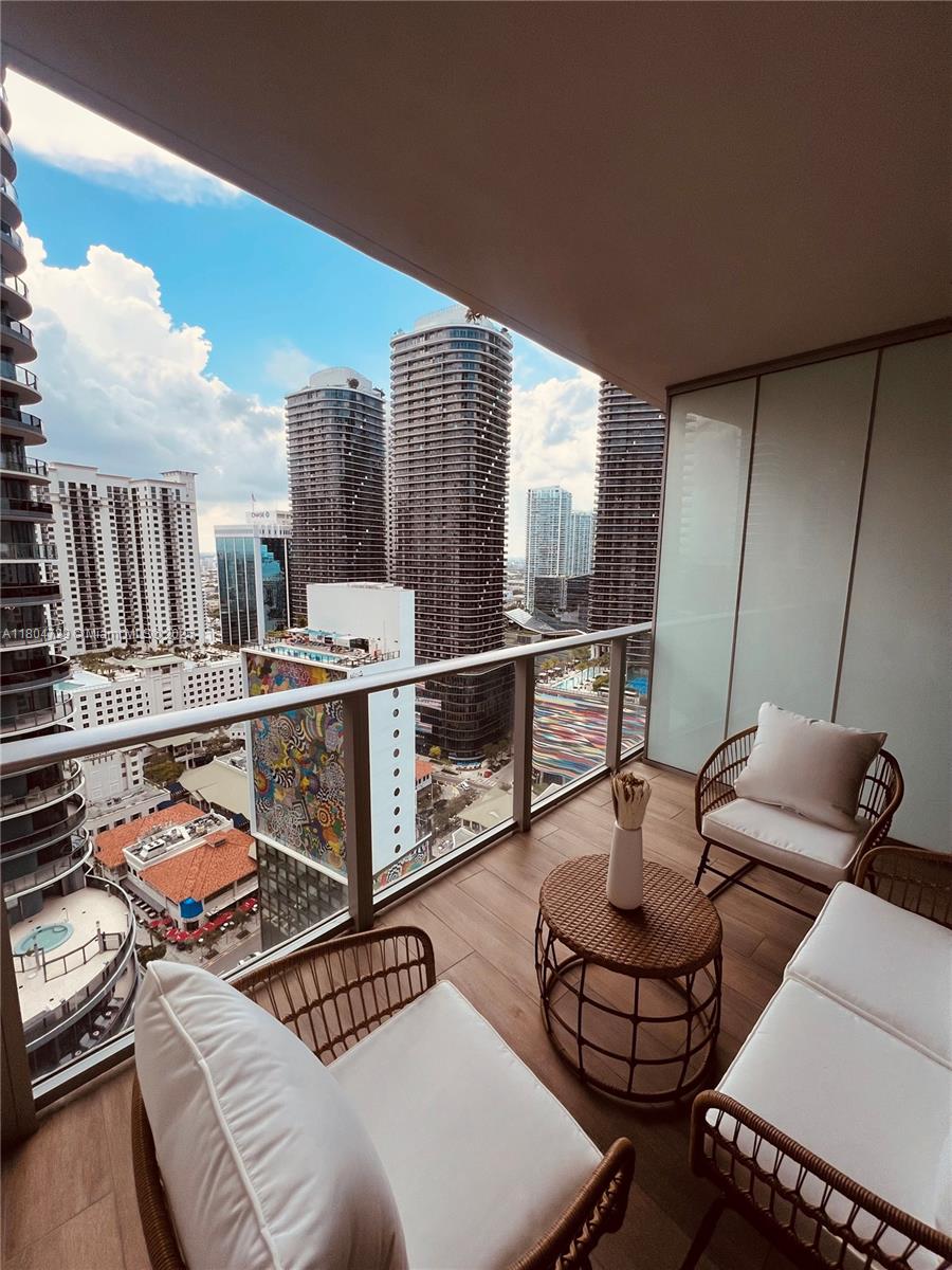 A balcony with wicker furniture overlooks a dense city skyline with several high-rise buildings — 1010 Brickell Ave # 2710, Miami FL 33131, MIAMI, FL