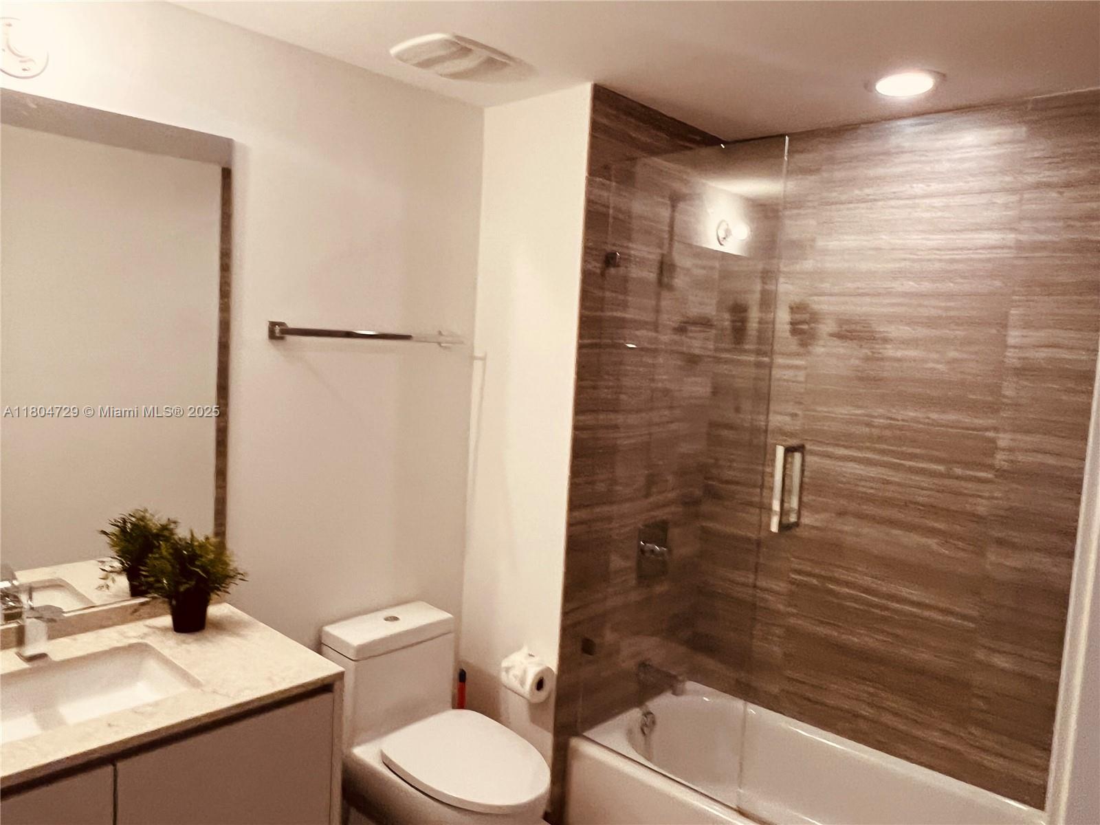A bathroom features a vanity, toilet, and a bathtub with a glass enclosure and tiled walls — 1010 Brickell Ave # 2710, Miami FL 33131, MIAMI, FL