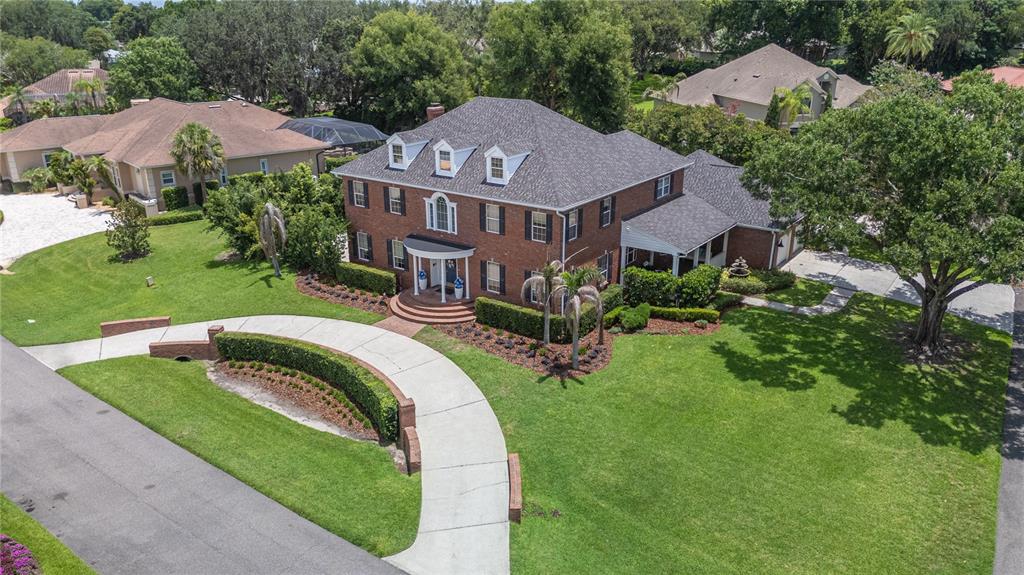 An aerial view of a two-story brick house with a curved driveway and landscaping — 5120 LAKE IN THE WOODS BOULEVARD, LAKELAND, FL