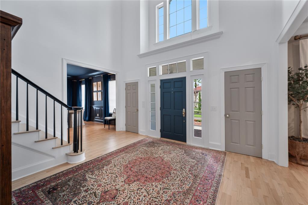 A two-story foyer features a dark blue front door, light wood floors, and a staircase — 5120 LAKE IN THE WOODS BOULEVARD, LAKELAND, FL