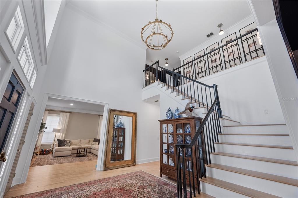 A two-story foyer features a wooden staircase, a large chandelier, and a view into a living room — 5120 LAKE IN THE WOODS BOULEVARD, LAKELAND, FL