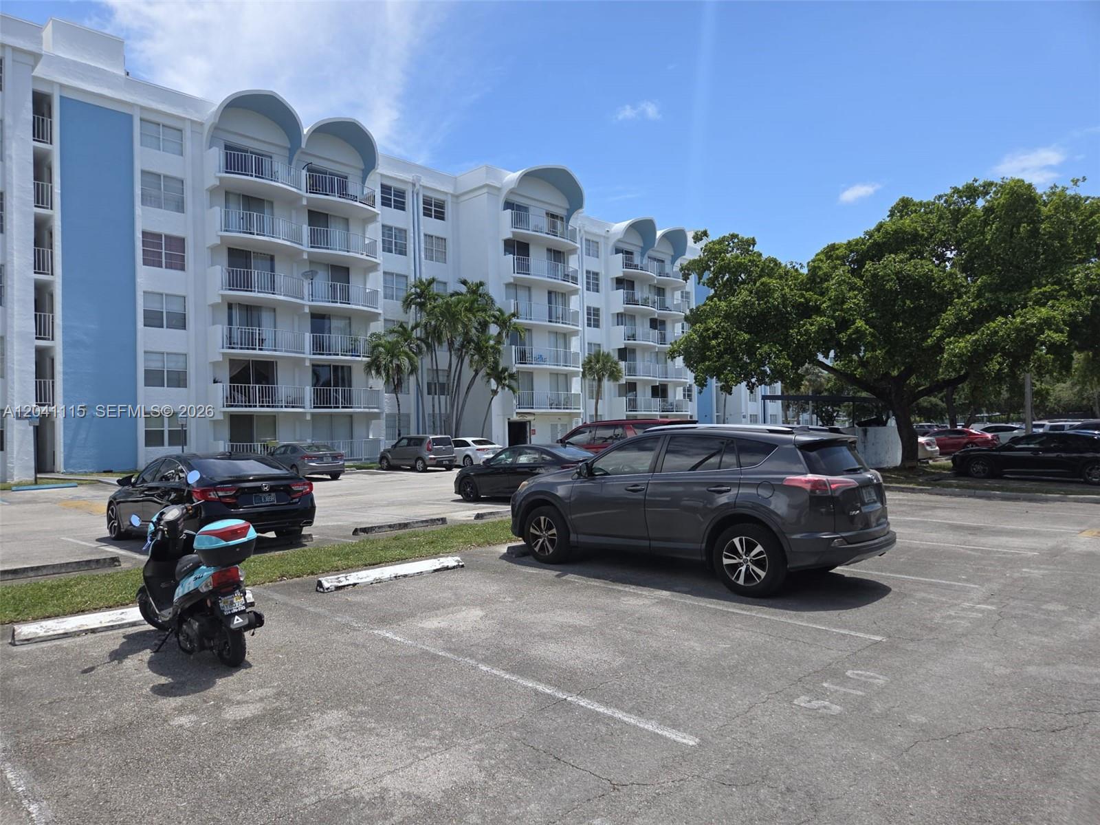 A multi-story apartment building with blue accents stands behind a paved parking lot — 496 NW 165th St Rd # 214, Miami FL 33169, MIAMI, FL
