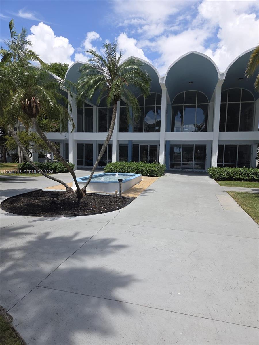 The exterior of a building features arched rooflines, large glass windows, and a small fountain — 496 NW 165th St Rd # 214, Miami FL 33169, MIAMI, FL