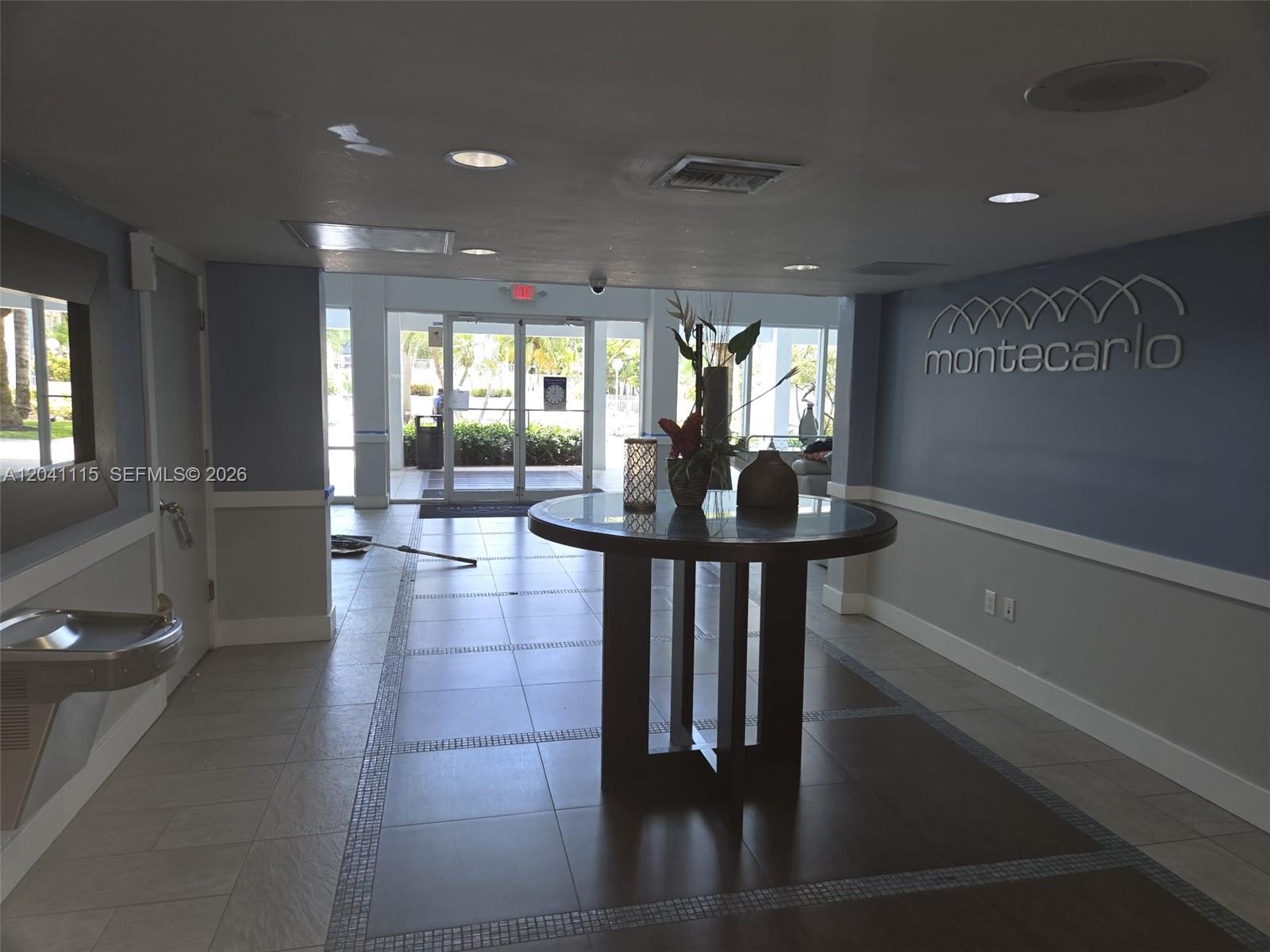 A lobby features a round center table, tiled floors, and a blue wall with signage — 496 NW 165th St Rd # 214, Miami FL 33169, MIAMI, FL