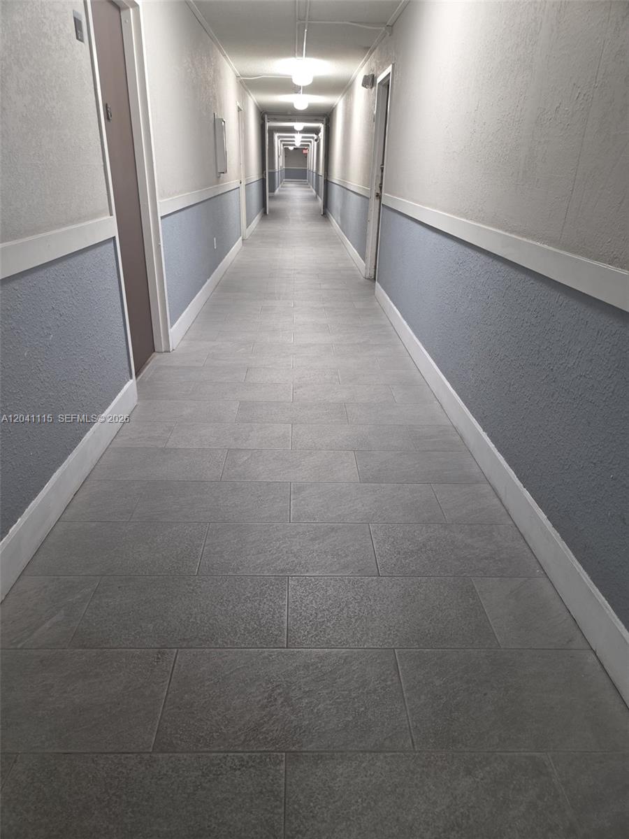 A long, narrow apartment hallway features gray tiled flooring and blue-painted lower walls — 496 NW 165th St Rd # 214, Miami FL 33169, MIAMI, FL