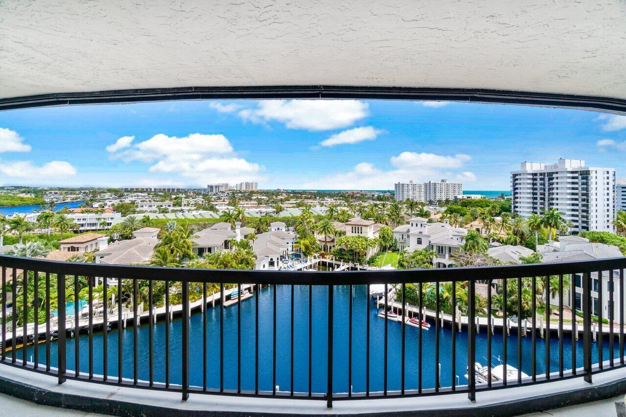 A balcony with a black railing overlooks a canal, residential homes, and distant high-rise buildings — 4740 S Ocean Boulevard # 903, Highland Beach FL 33487, HIGHLAND BEACH, FL