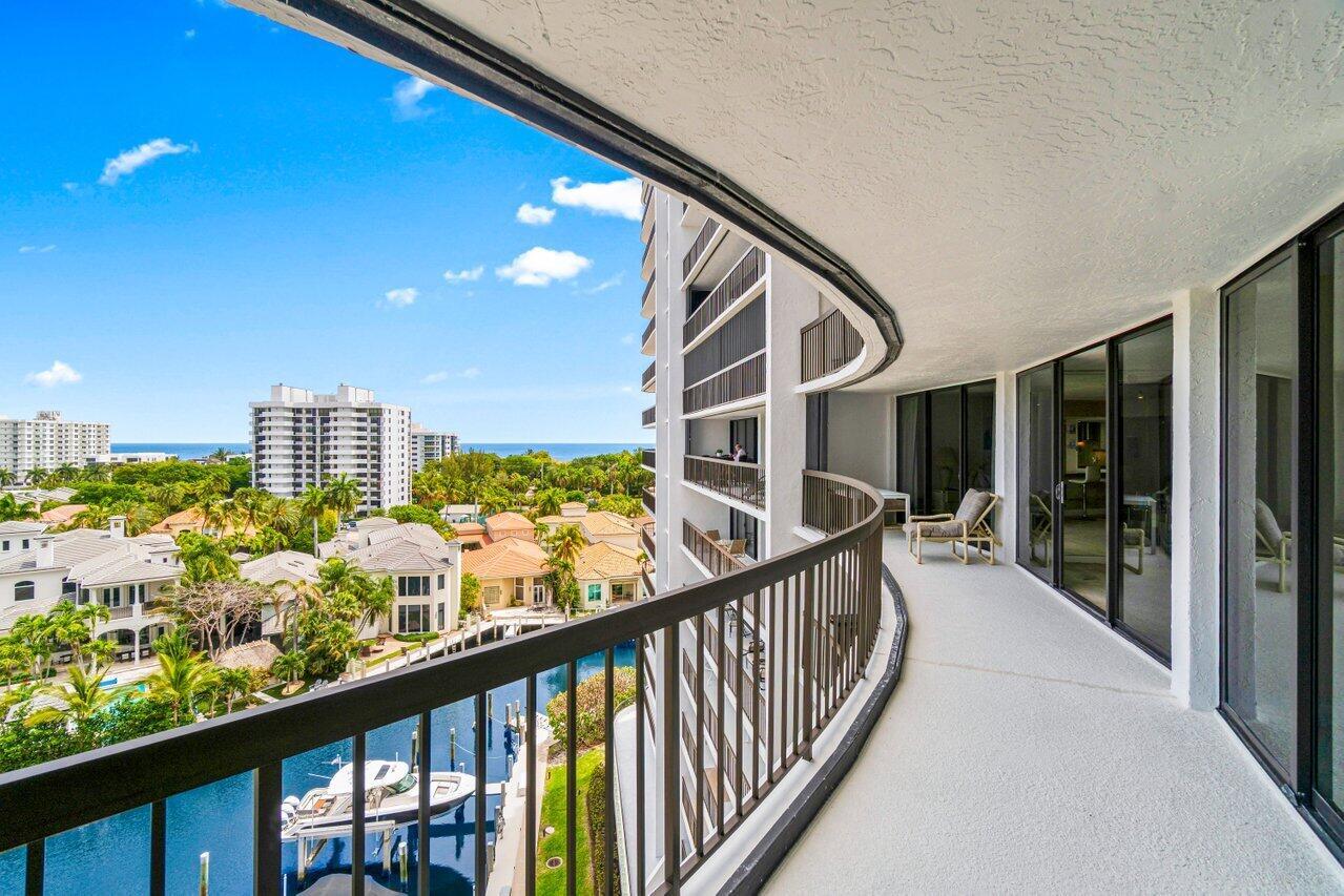 A curved balcony with metal railings overlooks a canal, residential homes, and the distant ocean — 4740 S Ocean Boulevard # 903, Highland Beach FL 33487, HIGHLAND BEACH, FL