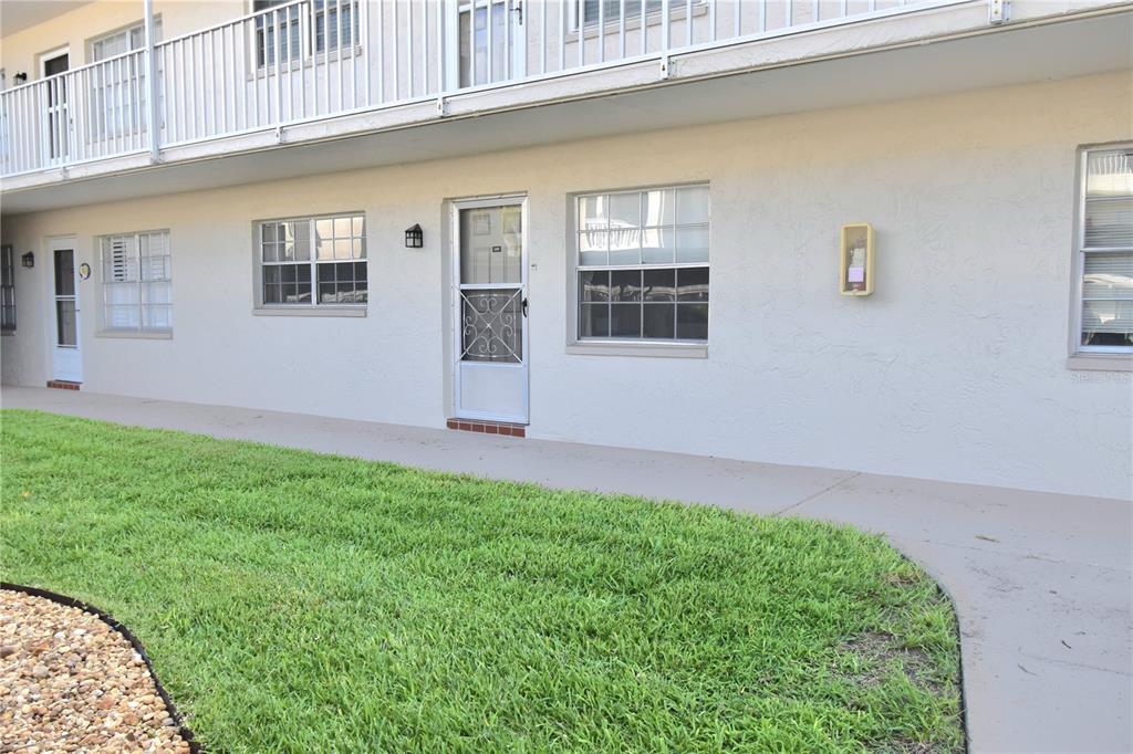 A ground-level apartment exterior with a white stucco wall, a screen door, and windows — 970 VIRGINIA STREET UNIT 107, DUNEDIN, FL