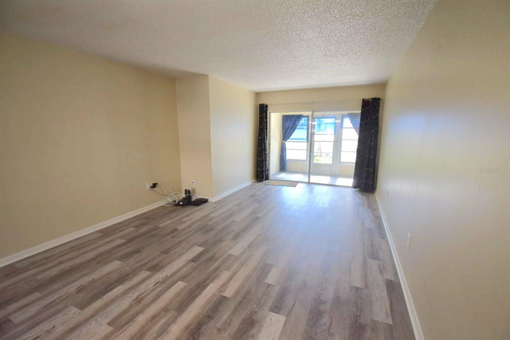 An empty living room with light-colored walls, wood-look flooring, and a sliding glass door — 970 VIRGINIA STREET UNIT 107, DUNEDIN, FL