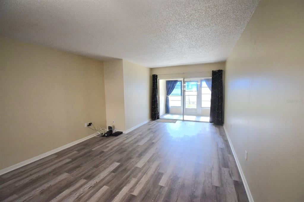 An empty living room features light-colored walls, wood-look flooring, and a sliding glass door — 970 VIRGINIA STREET UNIT 107, DUNEDIN, FL