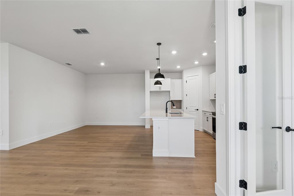 A modern kitchen with a white island and light wood flooring opens to a living area — 2808 MARRAKESH LANE, SARASOTA, FL