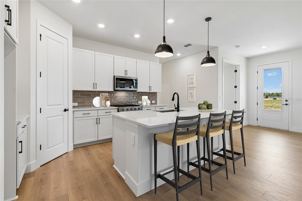 A modern kitchen features white cabinetry, a quartz-topped island with bar stools, and wood flooring — 2808 MARRAKESH LANE, SARASOTA, FL