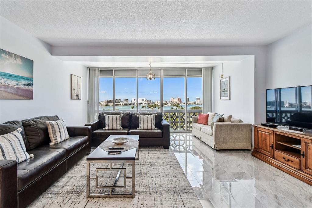 A living room features dark leather sofas, a beige sofa, and floor-to-ceiling windows overlooking water — 31 ISLAND WAY UNIT 609, CLEARWATER BEACH, FL