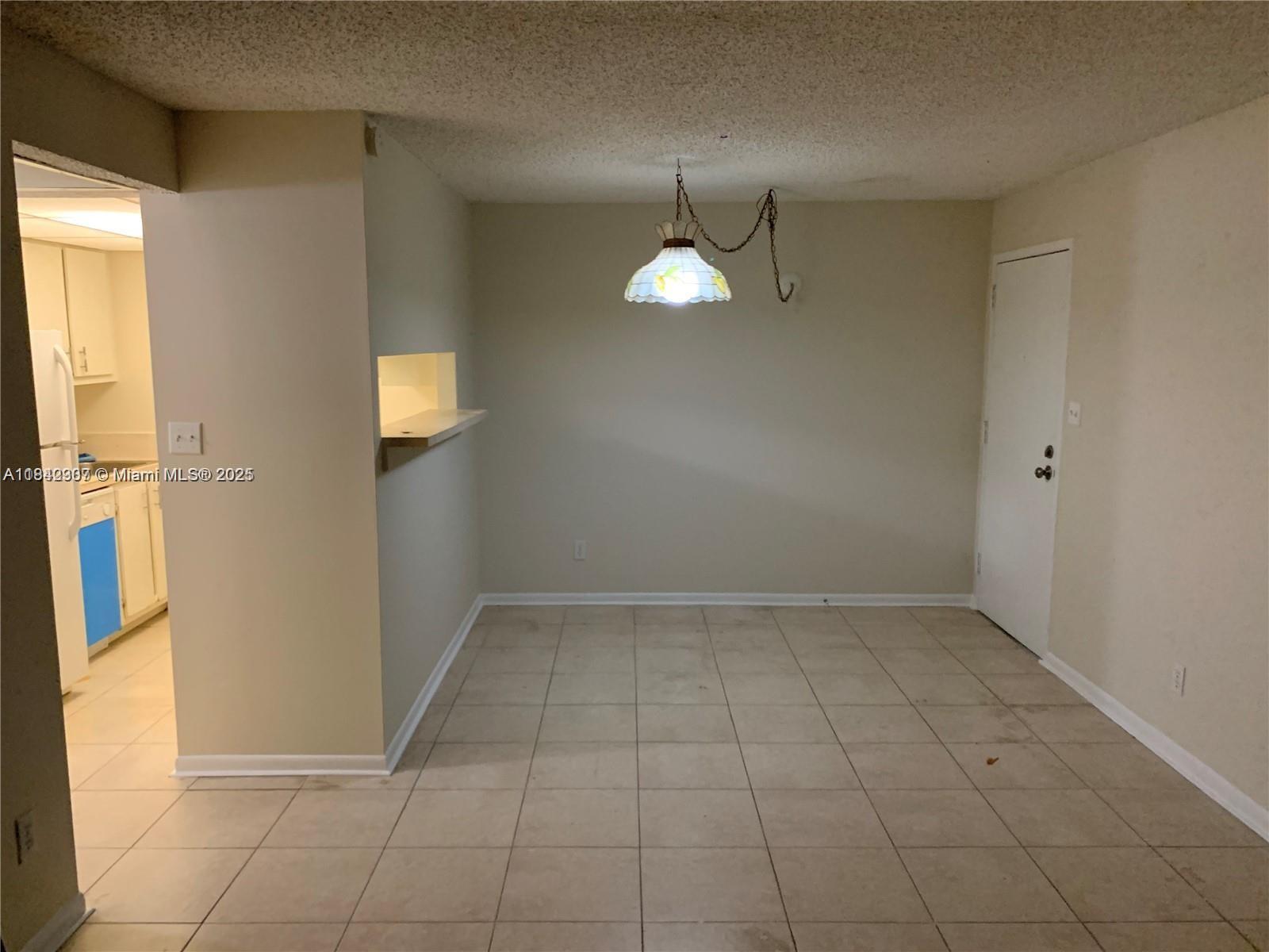 An empty dining area features beige tile flooring, a hanging pendant light, and a pass-through window — 5831 Washington St # 45, Hollywood FL 33023, HOLLYWOOD, FL