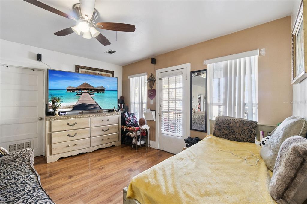 A bedroom features wood-look flooring, a ceiling fan, a large television on a dresser, and a bed — 310 E MAGNOLIA STREET, KISSIMMEE, FL