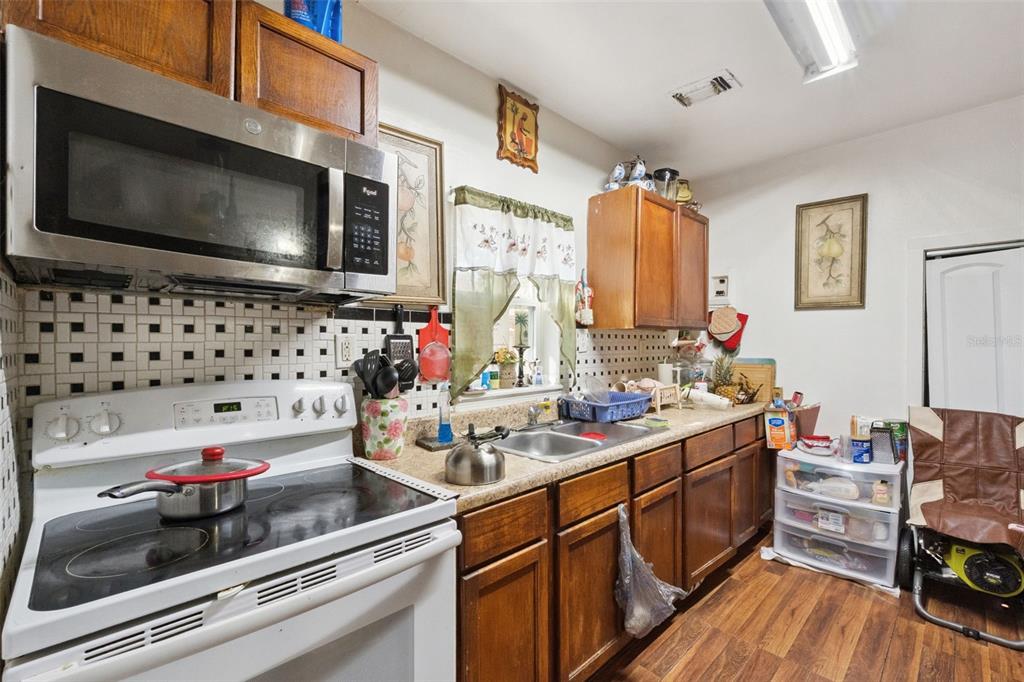A kitchen features wood cabinets, a white electric stove, a microwave, and a tiled backsplash — 310 E MAGNOLIA STREET, KISSIMMEE, FL