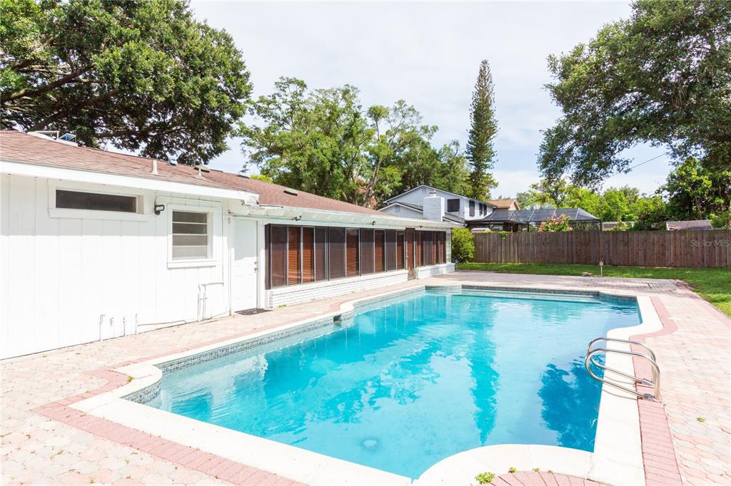 A backyard swimming pool sits adjacent to a white house with a screened-in porch — 11016 SAGINAW DRIVE, TAMPA, FL