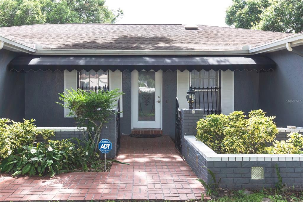 The exterior of a house features a brick walkway, a black awning, and gray walls — 11016 SAGINAW DRIVE, TAMPA, FL