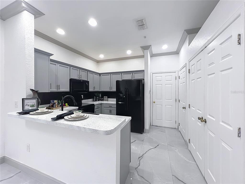 A kitchen features gray cabinets, black appliances, a breakfast bar, and white marble-look tile flooring — 14061 TURNING LEAF DRIVE, ORLANDO, FL