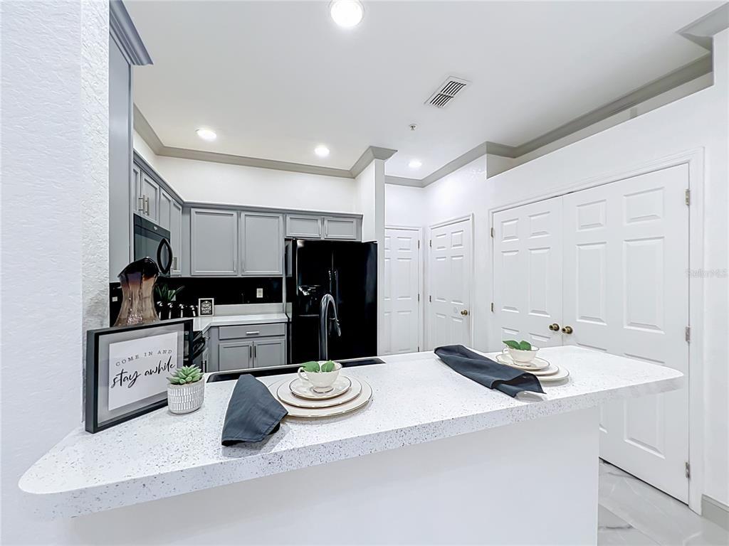 A kitchen features gray cabinets, a black refrigerator, and a white breakfast bar with stools — 14061 TURNING LEAF DRIVE, ORLANDO, FL