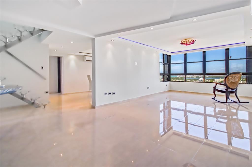A bright, open-concept living area features polished tile floors, a floating staircase, and floor-to-ceiling windows — 1715 COND. LA INMACULADA PLAZA I UNIT PH4, SAN JUAN, PR