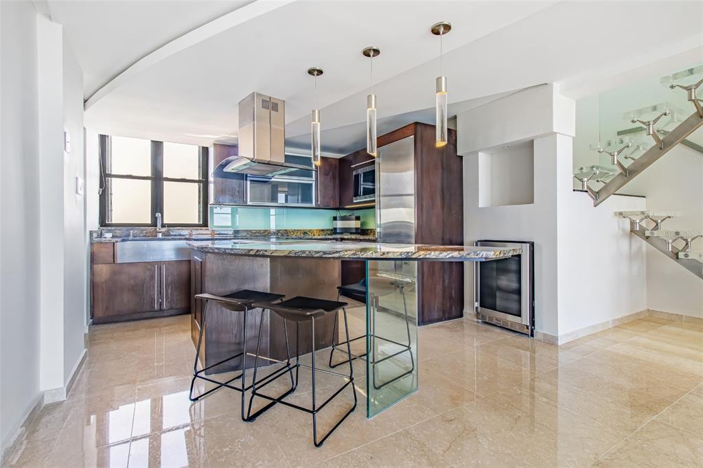 A modern kitchen features dark wood cabinetry, a glass-supported island, and a floating staircase — 1715 COND. LA INMACULADA PLAZA I UNIT PH4, SAN JUAN, PR