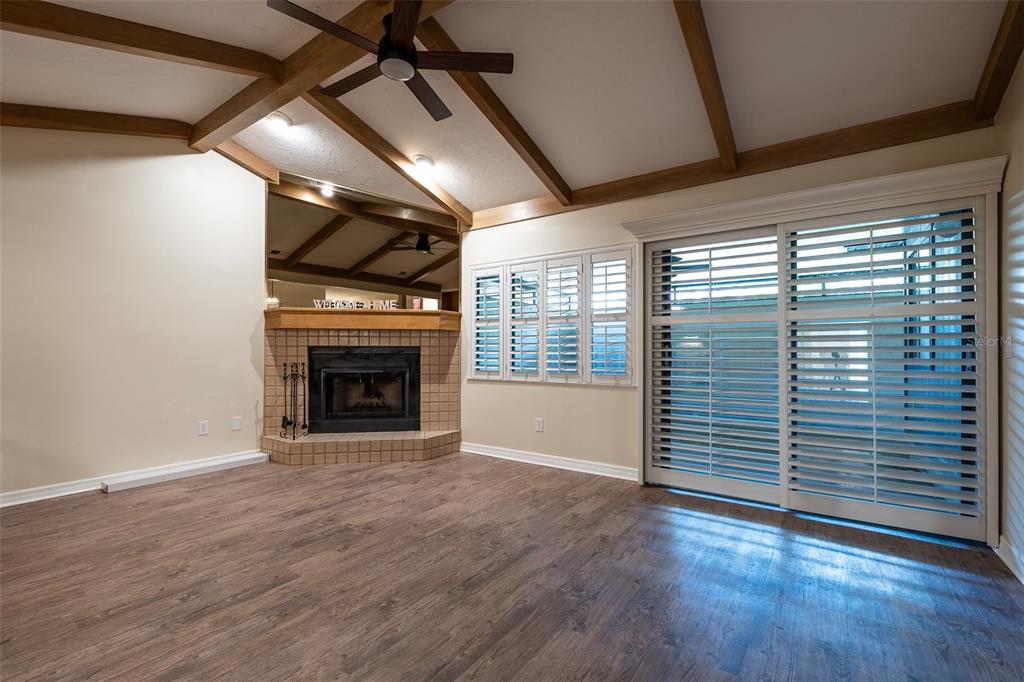 A living room features wood-look flooring, a corner fireplace, vaulted ceilings with beams, and shutters — 1720 NE 38 AVENUE, OCALA, FL
