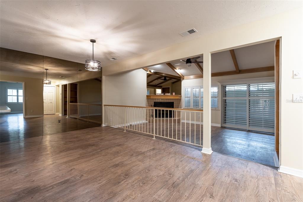 A living area with wood-look flooring, a mirrored wall, and a metal railing overlooking a den — 1720 NE 38 AVENUE, OCALA, FL
