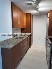A galley kitchen features wood cabinets, granite countertops, and stainless steel appliances — 10275 Collins Ave # 1435, Bal Harbour FL 33154, BAL HARBOUR, FL