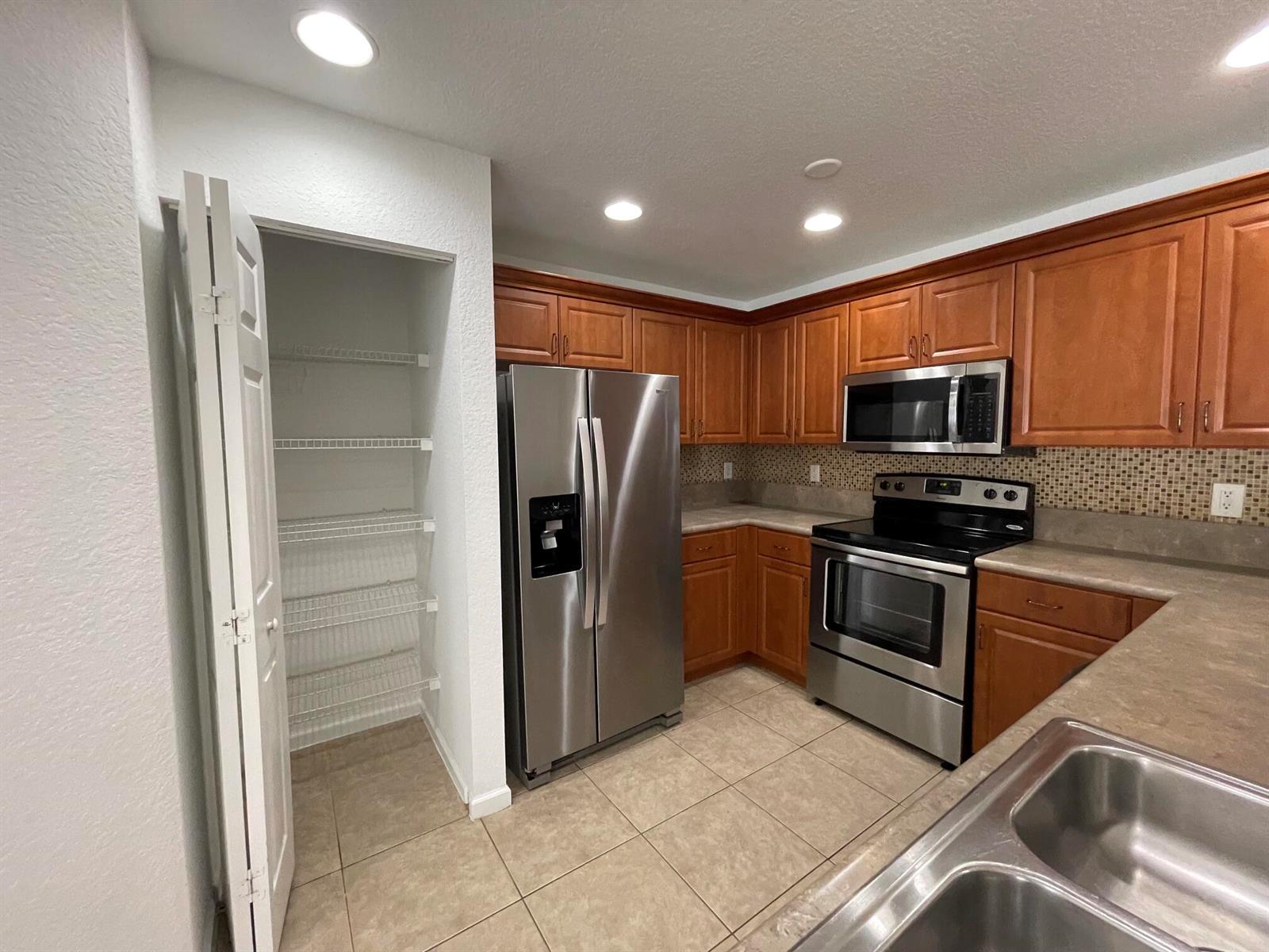 A kitchen features wood cabinets, stainless steel appliances, tile flooring, and a walk-in pantry — 6655 Duval Avenue, West Palm Beach FL 33411, WEST PALM BEACH, FL