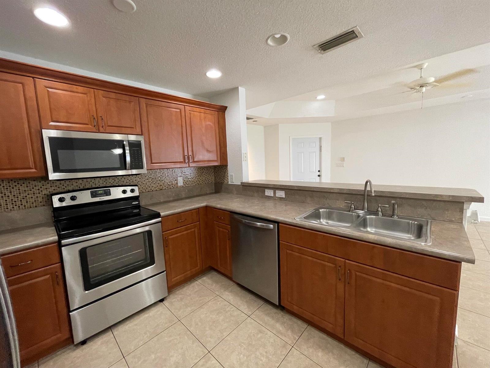 A kitchen with wood cabinets, stainless steel appliances, tile flooring, and a breakfast bar — 6655 Duval Avenue, West Palm Beach FL 33411, WEST PALM BEACH, FL
