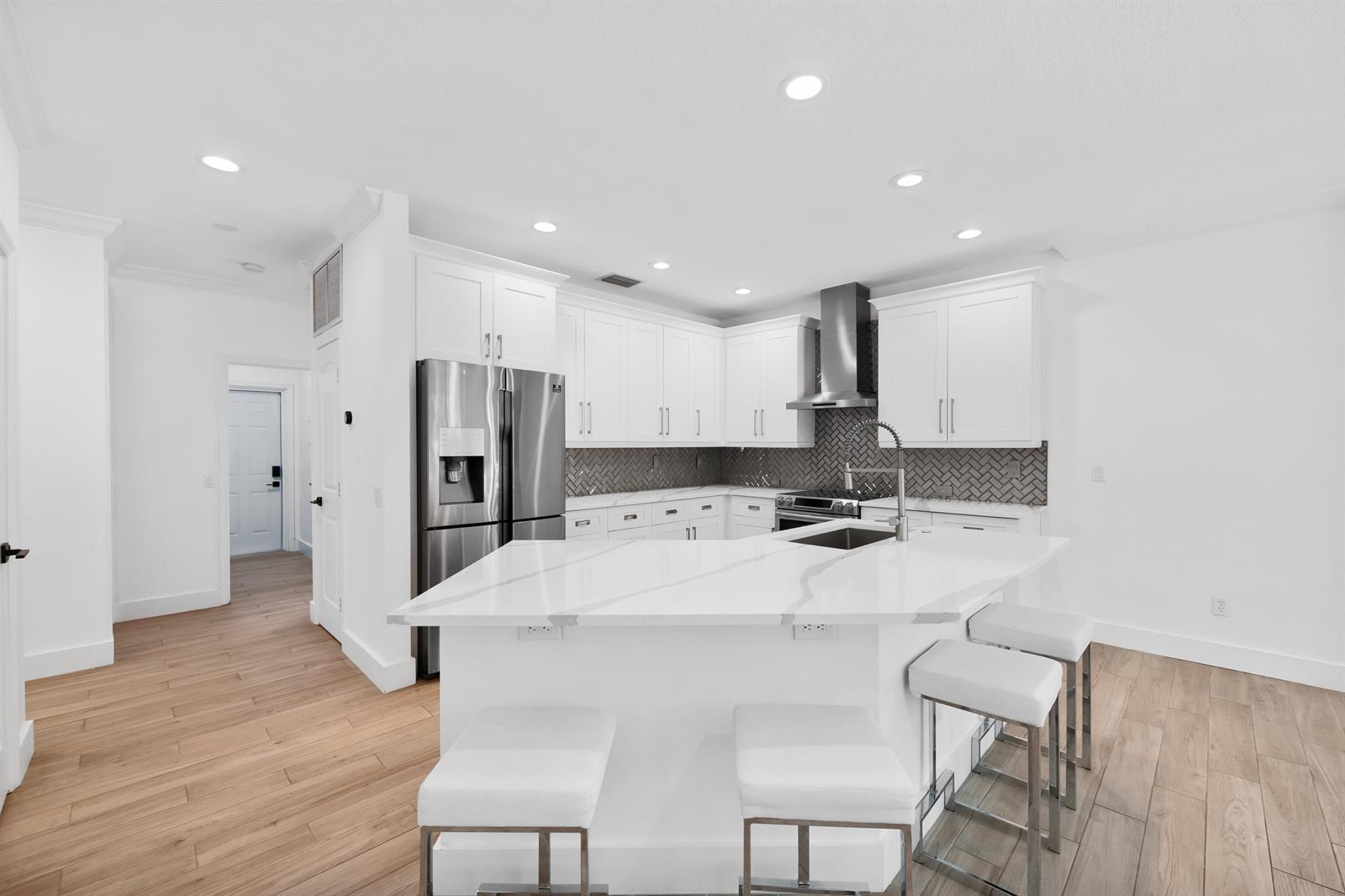 A modern kitchen features white cabinets, a marble-topped island with stools, and wood-look tile flooring — 10560 Walnut Valley Drive, Boynton Beach FL 33473, BOYNTON BEACH, FL