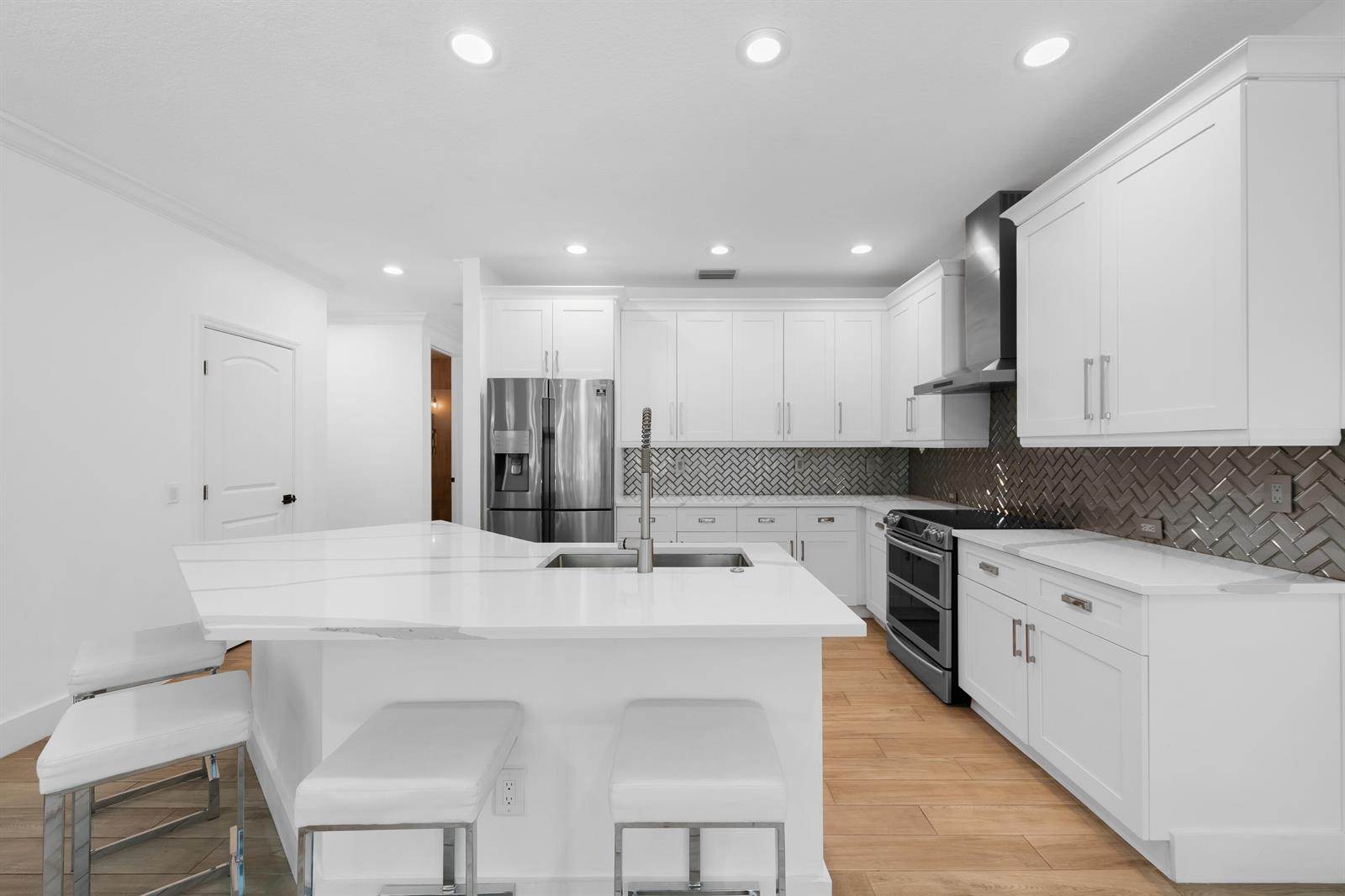 A modern kitchen features white cabinets, a large island with seating, and a herringbone backsplash — 10560 Walnut Valley Drive, Boynton Beach FL 33473, BOYNTON BEACH, FL