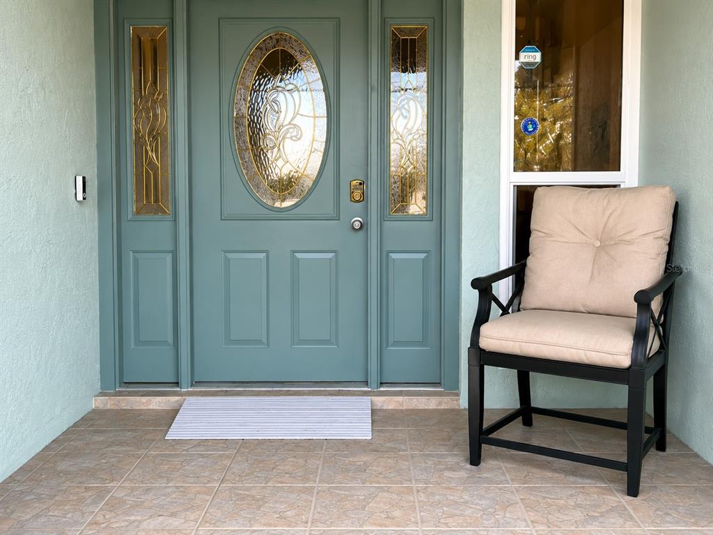 A teal front door with glass inserts sits next to a chair on a tiled porch — 11214 ROLLINGWOOD DRIVE, PORT RICHEY, FL