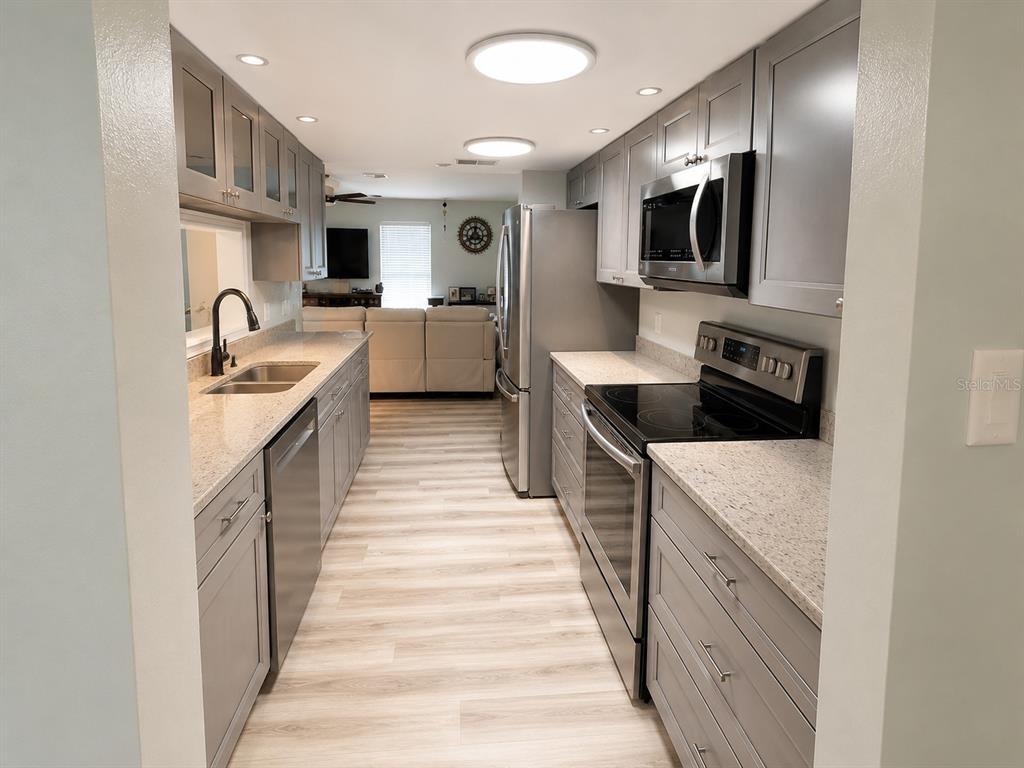 A galley kitchen features gray cabinets, stainless steel appliances, and light-colored granite countertops — 11214 ROLLINGWOOD DRIVE, PORT RICHEY, FL