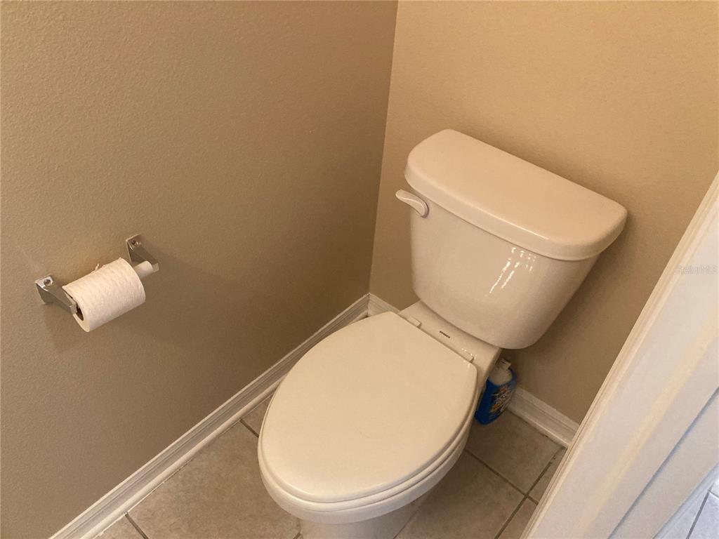 A white toilet sits in a bathroom with beige walls and light-colored tile flooring — 2533 HARN BOULEVARD UNIT 2, CLEARWATER, FL