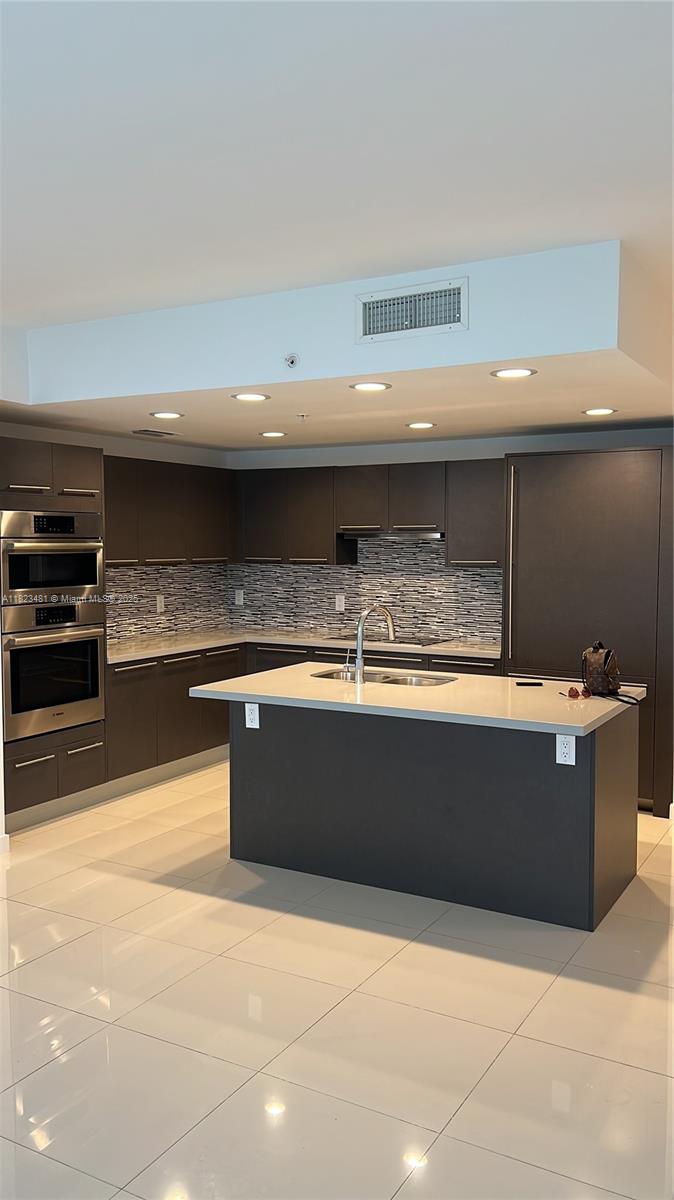 A modern kitchen features dark cabinetry, a central island with a sink, and light-colored flooring — 7661 NW 107th Ave # 207, Doral FL 33178, DORAL, FL