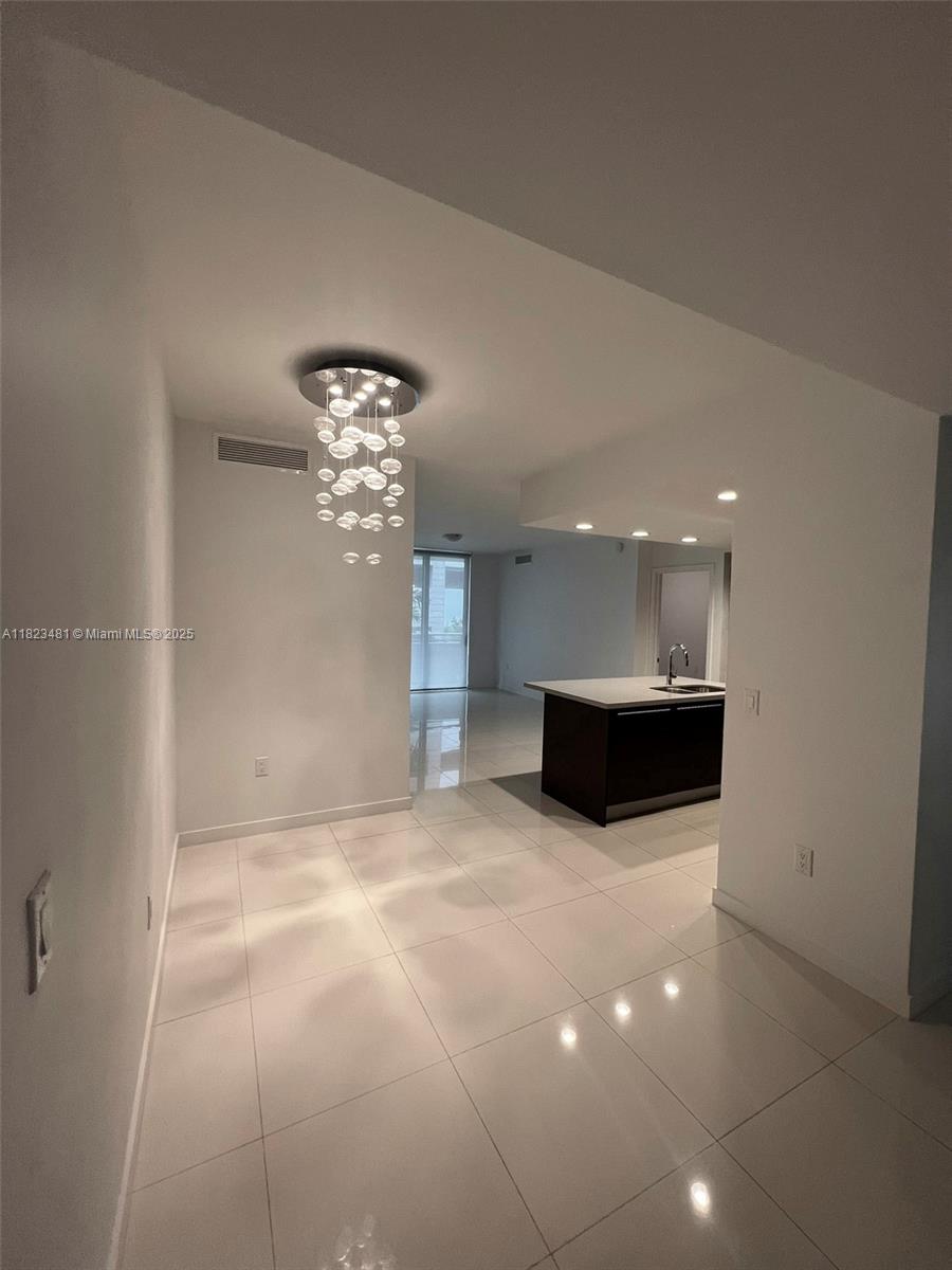 A modern dining area features a contemporary chandelier, white tile floors, and an open kitchen — 7661 NW 107th Ave # 207, Doral FL 33178, DORAL, FL