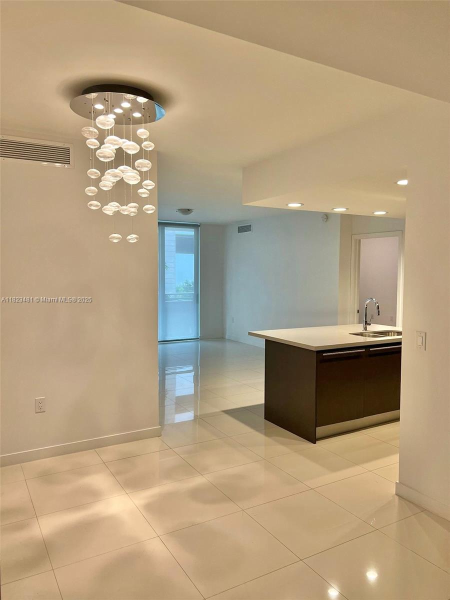 A modern kitchen with a dark island and white countertops sits adjacent to a living area — 7661 NW 107th Ave # 207, Doral FL 33178, DORAL, FL