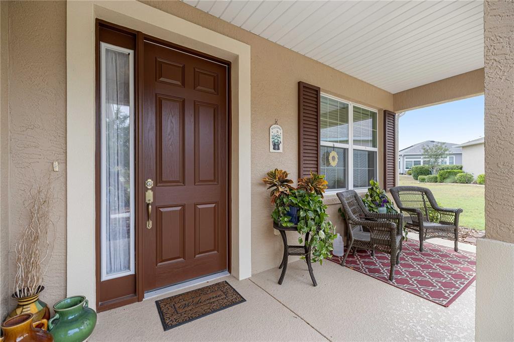A covered front porch features a brown door, two wicker chairs, and potted plants — 8237 SW 78TH TERRACE ROAD, OCALA, FL