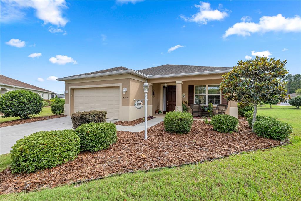 A single-story house with a tan stucco exterior, a two-car garage, and landscaped front yard — 8237 SW 78TH TERRACE ROAD, OCALA, FL