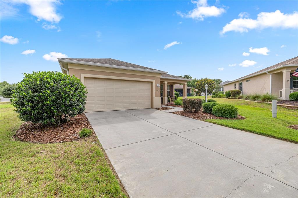 A beige single-story house features a two-car garage, a concrete driveway, and landscaped front yard — 8237 SW 78TH TERRACE ROAD, OCALA, FL