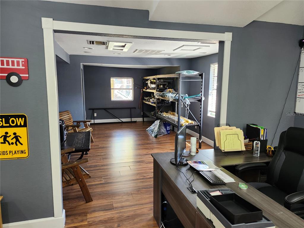 A home office with wood-look flooring, a desk, and an adjacent room with storage shelving — 1901 W SLIGH AVENUE, TAMPA, FL